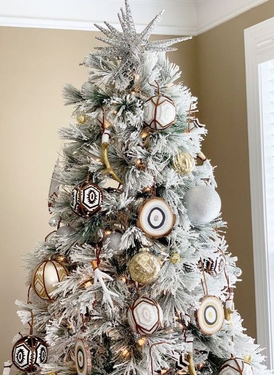 a flocked Christmas tree with white glitter ornaments, gold ones, agate slices and gold antlers plus lights is very free-spirited