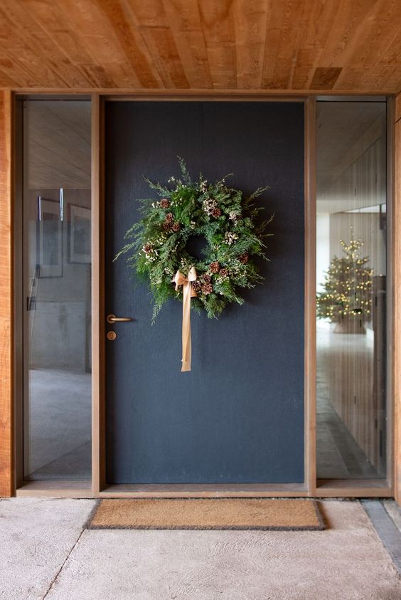a lush modern Christmas wreath with lush greenery, some white blooms, pinecones and a peachy pink ribbon bow