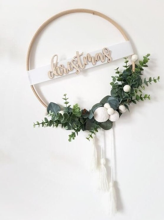 a modern Christmas wreath of an embroidery hoop, greenery, white pompoms and white tassels