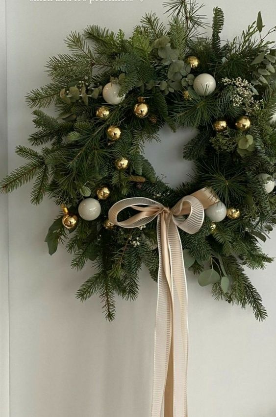 a modern Christmas wreath of evergreens and eucalyptus, white and gold ornaments and a ribbon bow is super cool