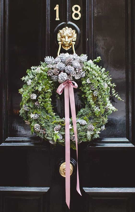 a modern Christmas wreath of greenery, evergreens, snowy pinecones and a pink ribbon bow is a cool idea