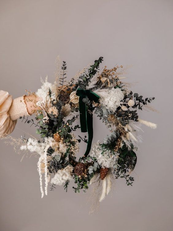 a modern boho Christmas wreath with dried grasses, leaves, pinecones and faux berries and a green bow on top