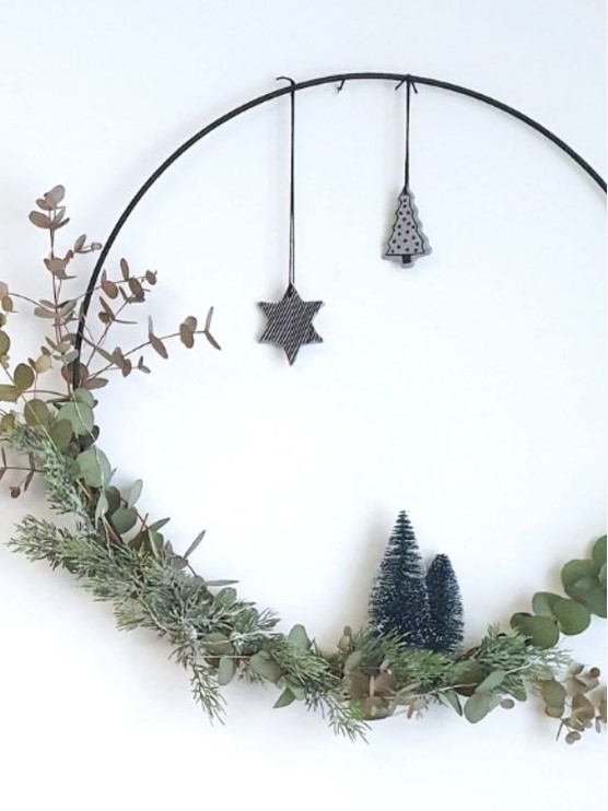 a modern meets Scandi Christmas wreath with greenery, leaves, bottle brush trees and some plywood ornaments hanging