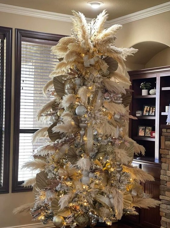 a pampas grass Christmas tree decorated with large metallic ornaments, lights and fronds and topped with some branches