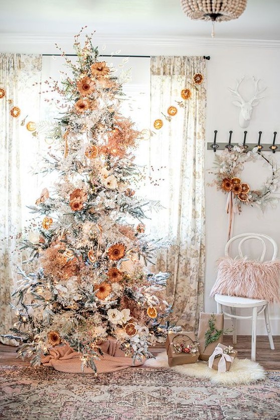 a pretty boho natural Christmas tree decorated with lights, dried and fabric blooms, blooming branches and berries and some burlap at the base