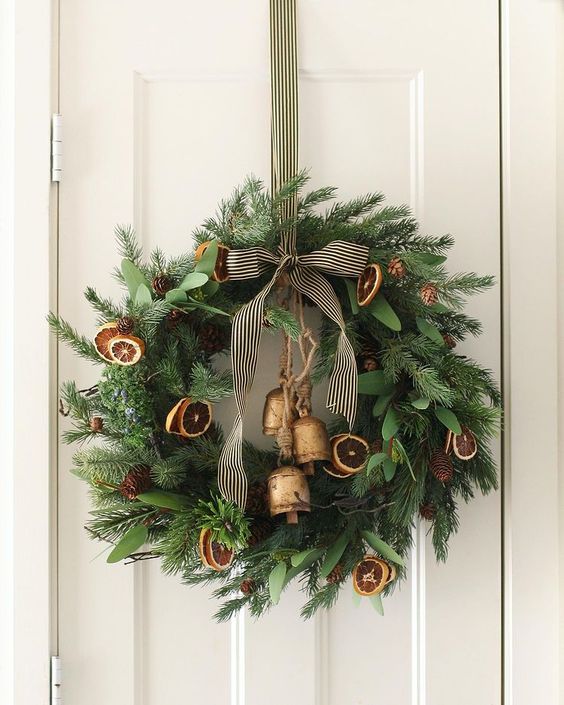 a pretty modern Christmas wreath of evergreens, dried citrus, bells and a striped ribbon is a cool and catchy idea