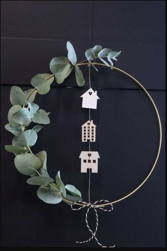 a simple modern Christmas wreath with eucalyptus, plywood houses and yarn is a cool and catchy idea
