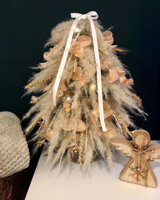 a small tabletop pampas grass Christmas tree decorated with wheat and some leaves plus lights and a bow for a boho space