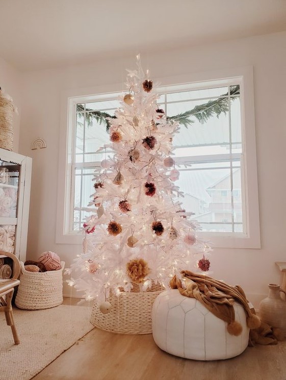 a white Christmas tree decorated with fluffy pompoms of earthy colors and put into a basket to make it look a bit rustic