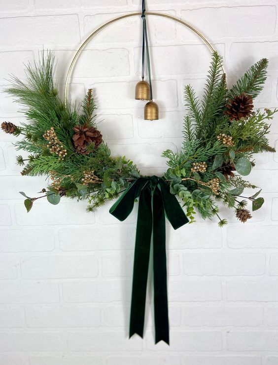an elegant modern Christmas wreath with evergreens, greenery, branches, pinecones, berries, vintage bells and a dark green bow