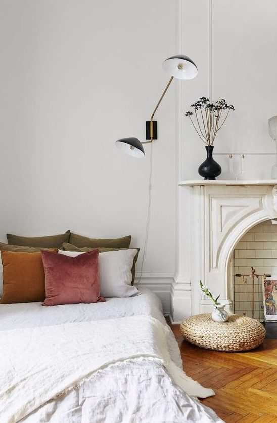 a beautiful Parisian bedroom with a faux fireplace, art deco lamps, a bed with muted pillows