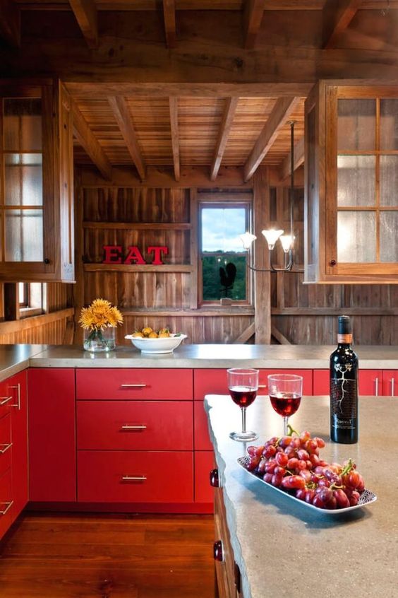 a bold chalet kitchen with red lower cabinets, stained wooden walls, a wood and stone kitchen island and lovely views