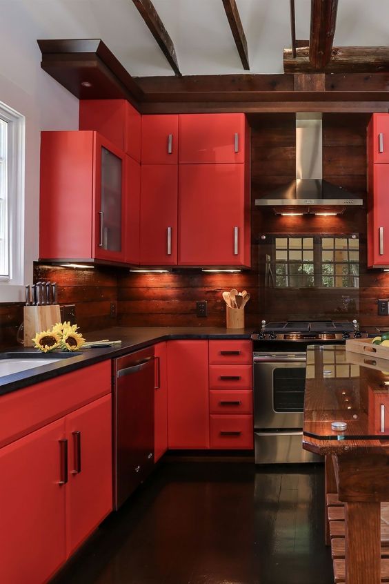 a bold red kitchen with a stained wood backsplash, black countertops, stainless steel appliances and built-in lights