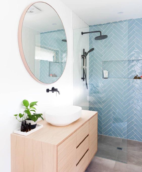 a chic modern bathroom with a blue herringbone tile accent wall, a stained vanity, a round mirror and black fixtures