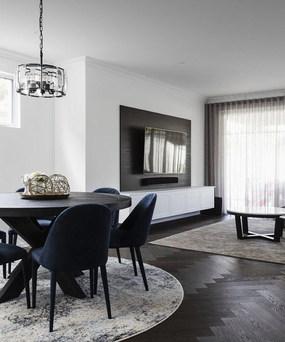 a chic modern space with white walls and a dark-stained herringbone floor, a dark table and navy chairs, a coffee table