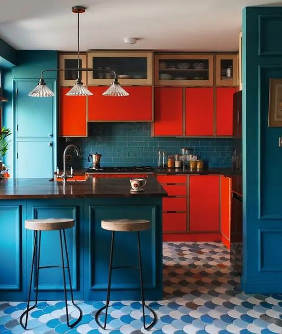 a colorful kitchen with bright red cabinets, navy cabinets, walls and a backsplash plus a retro pendant lamp and a scallop tile floor