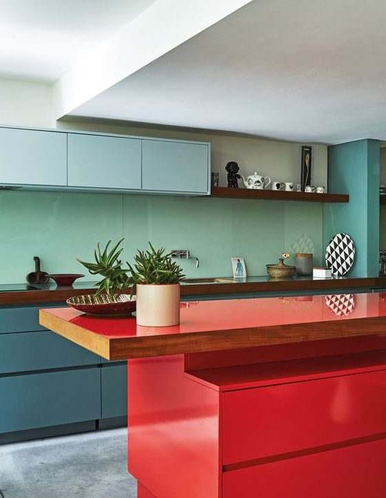 a colorful kitchen with sleek cabinetry in light blue, slate blue and with a bold red kitchen island and a sleek aqua-colored backsplash