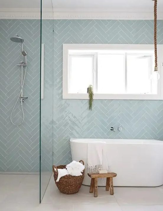 a contemporary bathroom with dusty blue herringbone tiles, an oval tub, a shower, a basket and a stool is welcoming