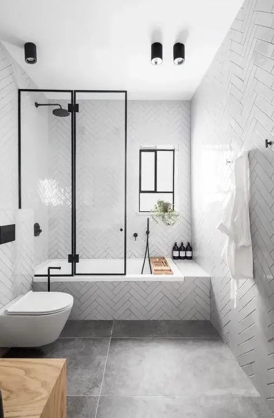 a contemporary bathroom with glossy white tiles, large scale tiles on the floor, black fixtures and a window for more light
