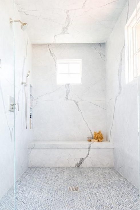 a fresh shower space with white marble and little herringbone clad tiles on the floor plus a window