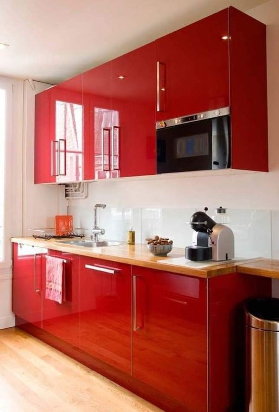 a glossy red kitchen with a clear glass backsplash and butcherblock countertops, built-in appliances is wow