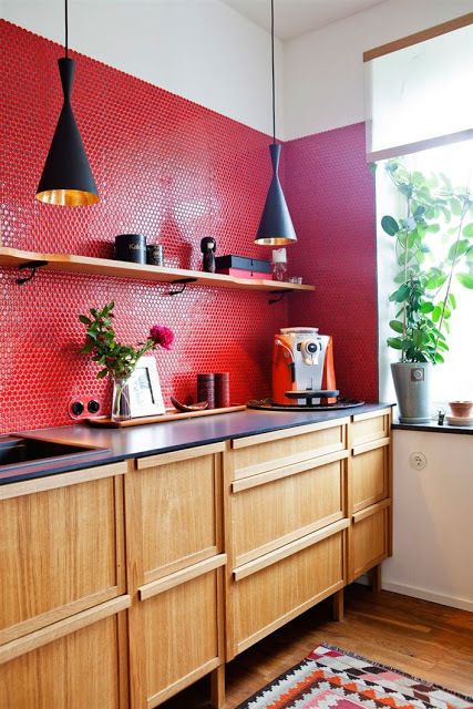 a light-stained kitchen with black countertops, a red penny tile backsplash and black pendant lamps and blooms