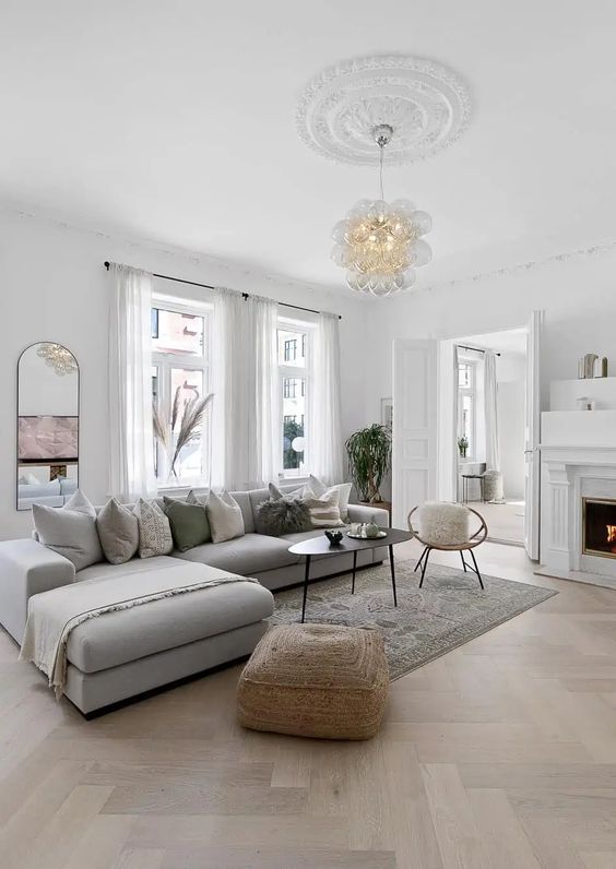a lovely and cozy living room with a herringbone floor, a fireplace, a low grey sofa, a coffee table and some decor
