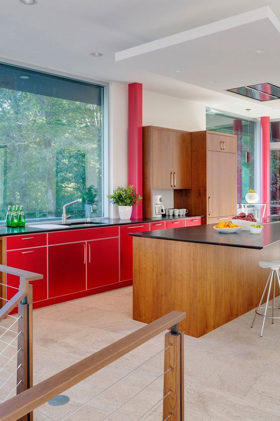 a mid-century modern kitchen with bright red and stained cabinets, a large window instead of a backsplash and black countertops