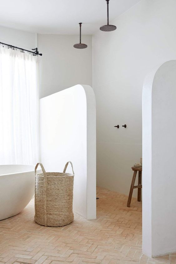 a minimal bathroom with white walls and a terracotta tile herringbone floor, a shower space and an oval tub