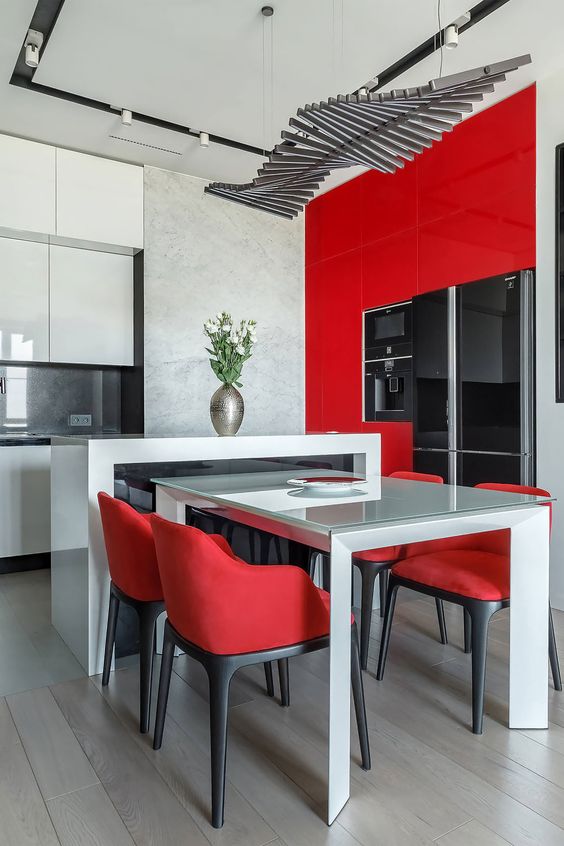 a minimalist red and white glossy kitchen with a sculptural kitchen island and a table, red chairs and a creative chandelier