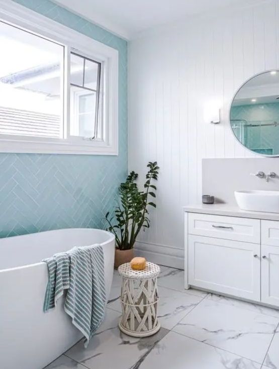 a modern coastal bathroom with a white planked and turquoise herringbone tile wall, a white marble floor, a white vanity and tub