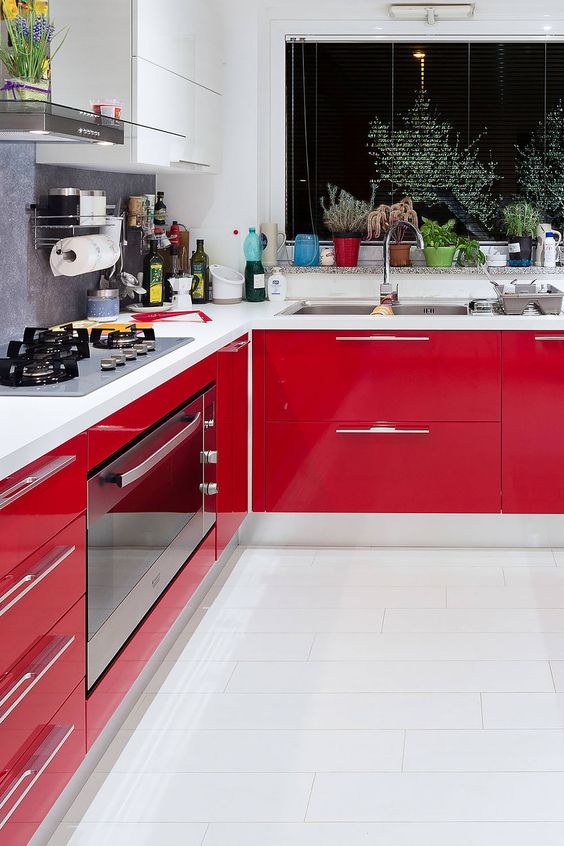 a modern kitchen with glossy red and matte white cabinets, white countertops, potted plants and stainless steel appliances