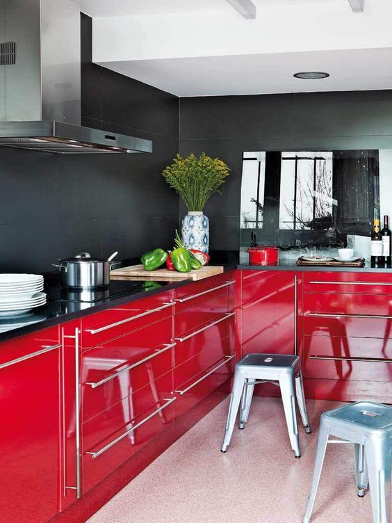 a moody kitchen with black walls and glossy red lower cabinets for a contrast, metallic stools and a glass backsplash