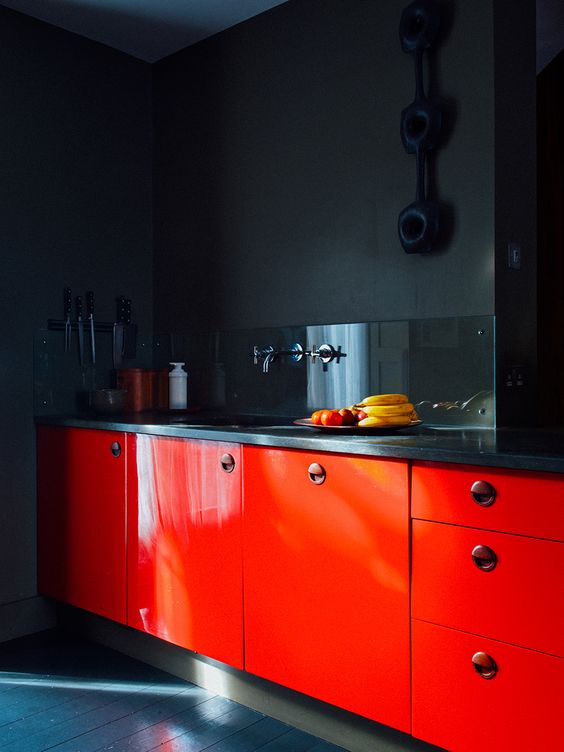 a moody soot kitchen with red cabinets, black countertops and a glossy black backsplash is a catchy and unique space