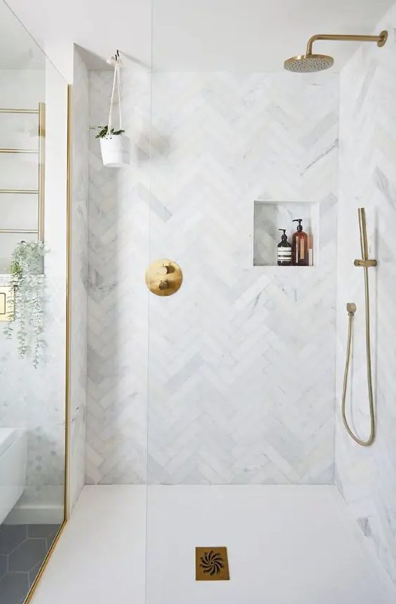 a neutral bathroom with penny and herringbone tiles, a niche, some brass touches and potted plants