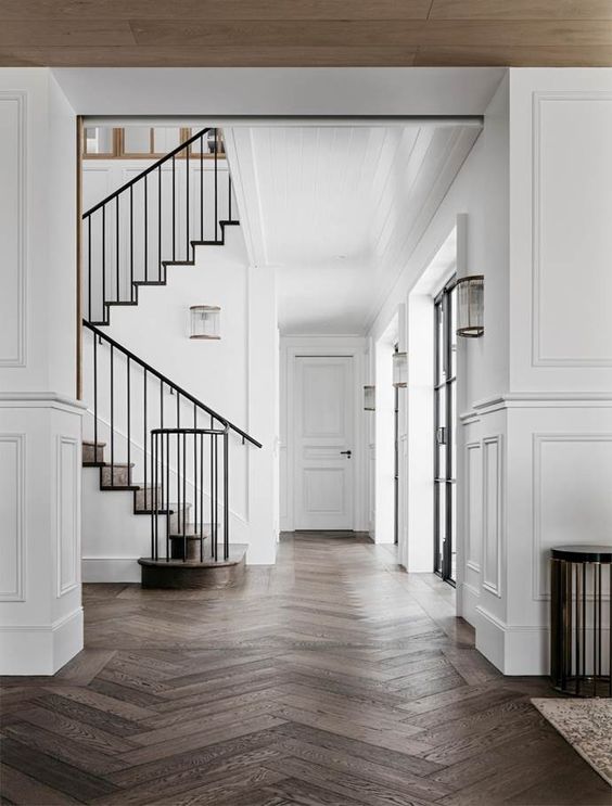 a refined space with white walls with molding and dark-stained herringbone floors, black railing is super chic