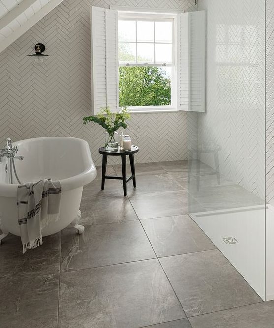 a small attic bathroom with herringbone and large format tiles, a clawfoot tub, a shower space, shutters and a black stool