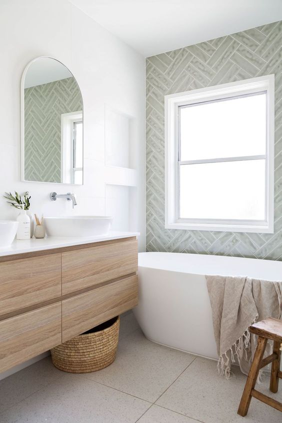 a small neutral bathroom with grey herringbone tiles, a stained floating vanity, an oval tub and a wooden stool