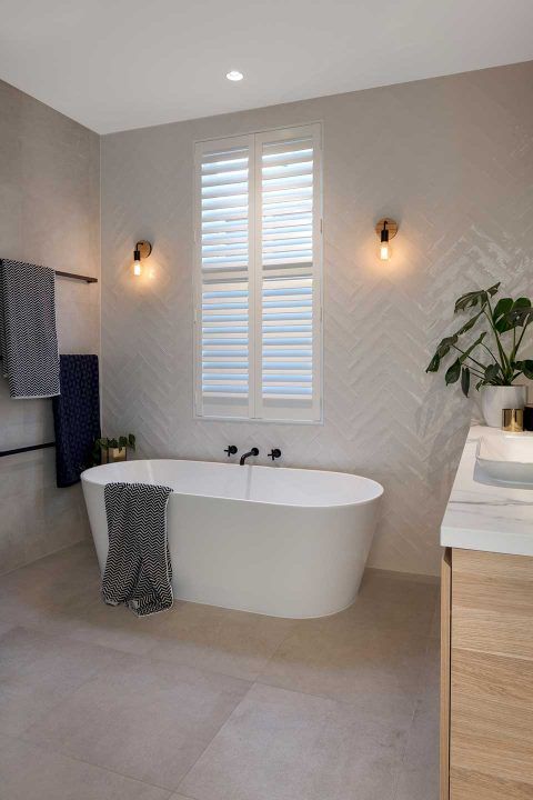 a soothing bathroom with white herringbone tiles and large scale ones on the floor, a tub, a stained vanity and grey towels