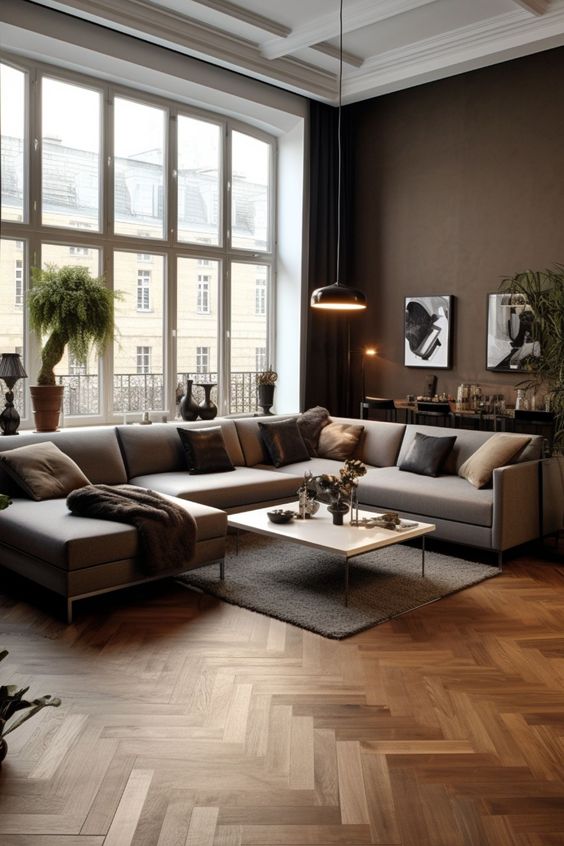 a sophisticated living room with chocolate brown walls, a large window, a grey sectional, a herringbone floor and bold artwork