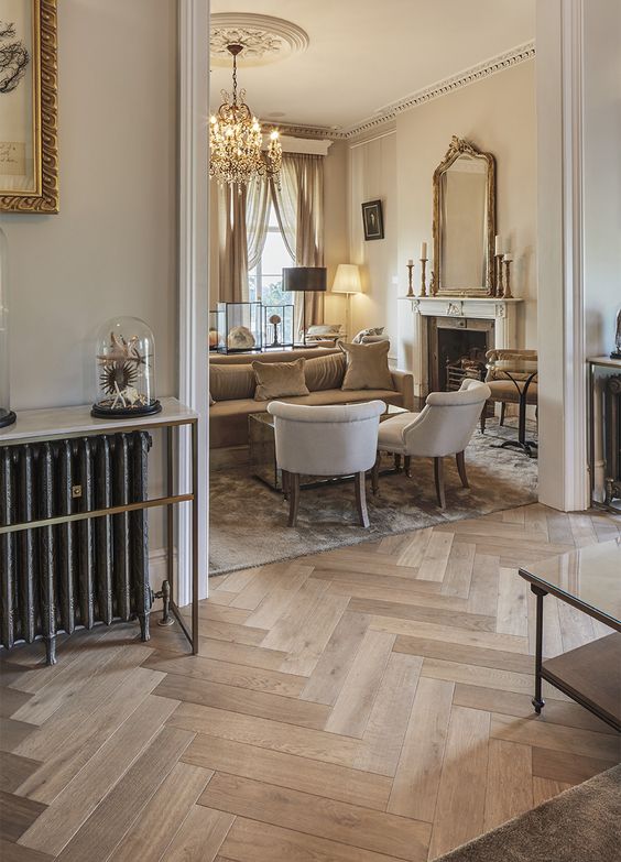 a sophisticated neutral space with light-stained herringbone floors, neutral seating furniture, a fireplace and some lamps