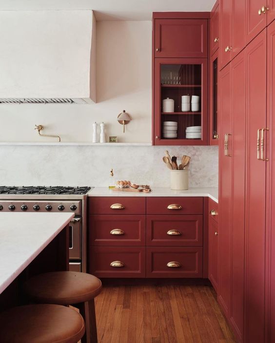 a sophisticated vintage red kitchen with shaker cabinets, a white backsplash and countertops and a large hood