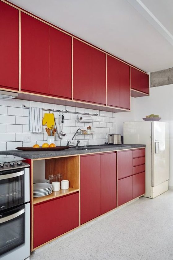 a stylish bold mid-century modern kitchen with red plywood cabinets and a white subway tile backsplash and a white fridge