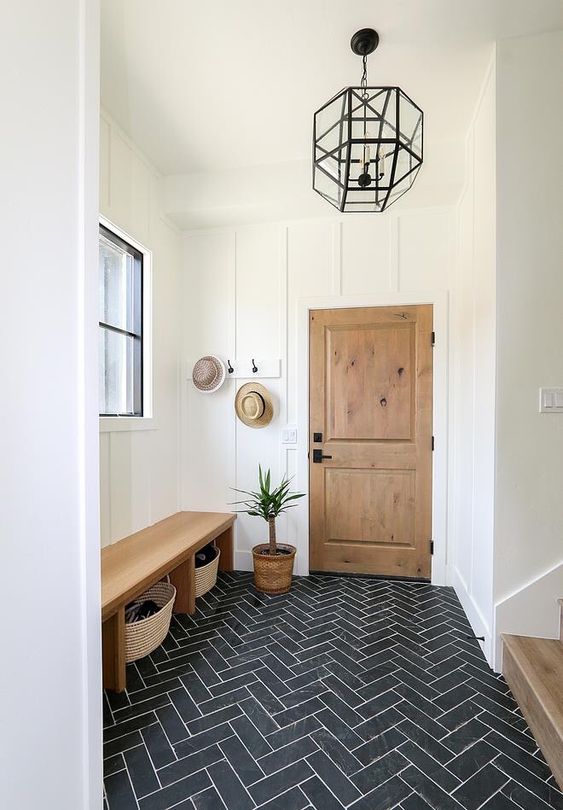 a stylish farmhouse entryway with white molded walls, a graphite grey herringbone floor, a bench with baskets