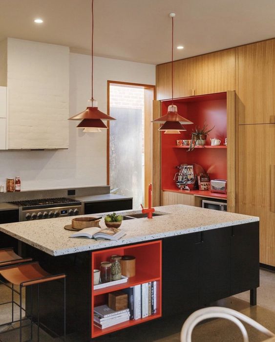 a stylish retro kitchen with a stained storage unit, red backing, a black kitchen island with a red shelving unit, red pendant lamps