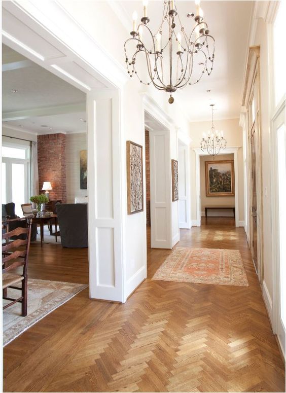a welcoming space with white molded walls, stained herringbone floors, dark-stained furniture and chic chandeliers