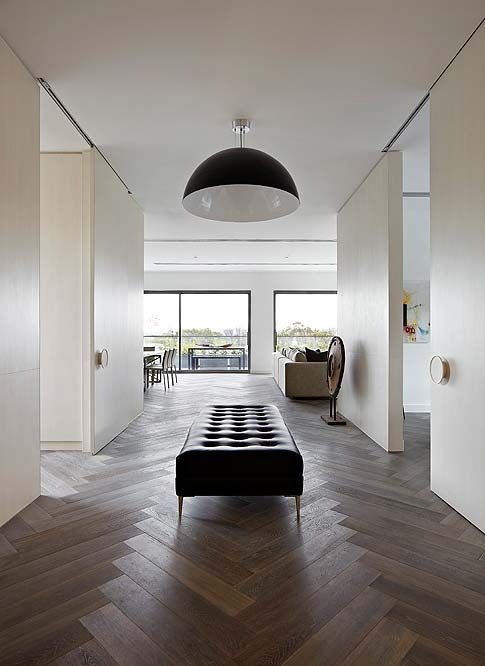 an airy and vast space done with neutral walls and a dark herringbone floor, a black lamp and a black ottoman