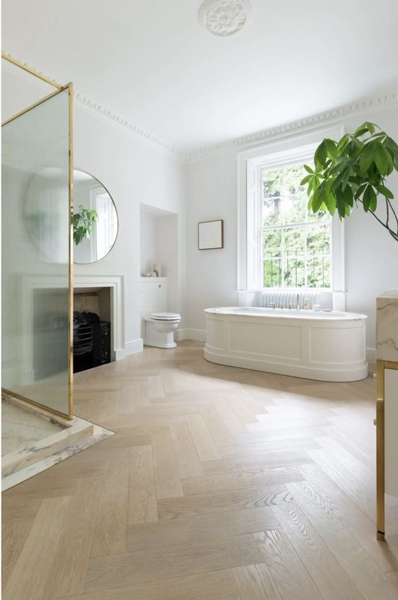 an exquisite bathroom with a fireplace, a herringbone floor, an oval tub, a shower and some plants