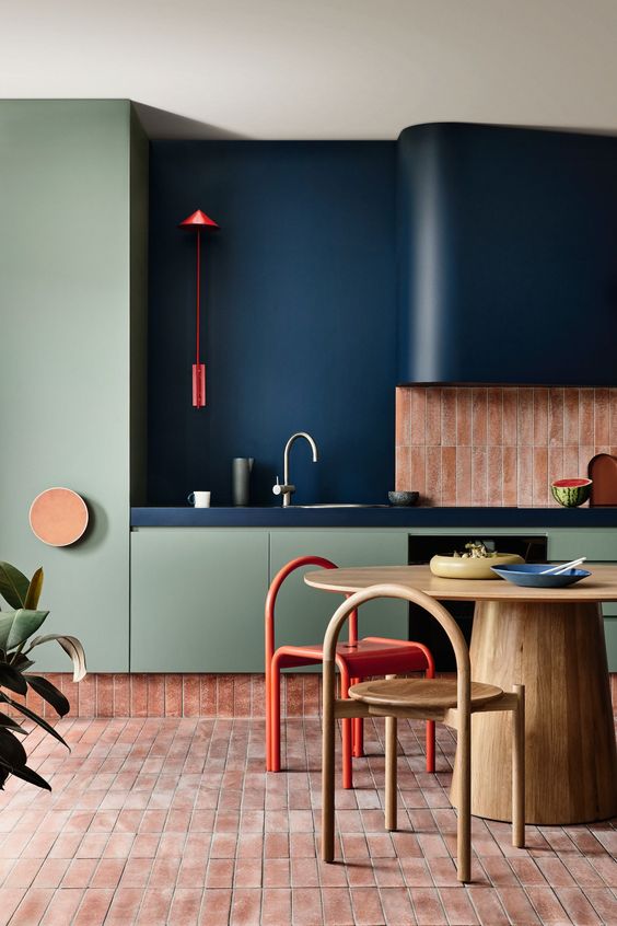 a bold kitchen with olive green cabinetry, a navy and pink stacked tile backsplash, a navy hood, a stained table and a pink tile floor