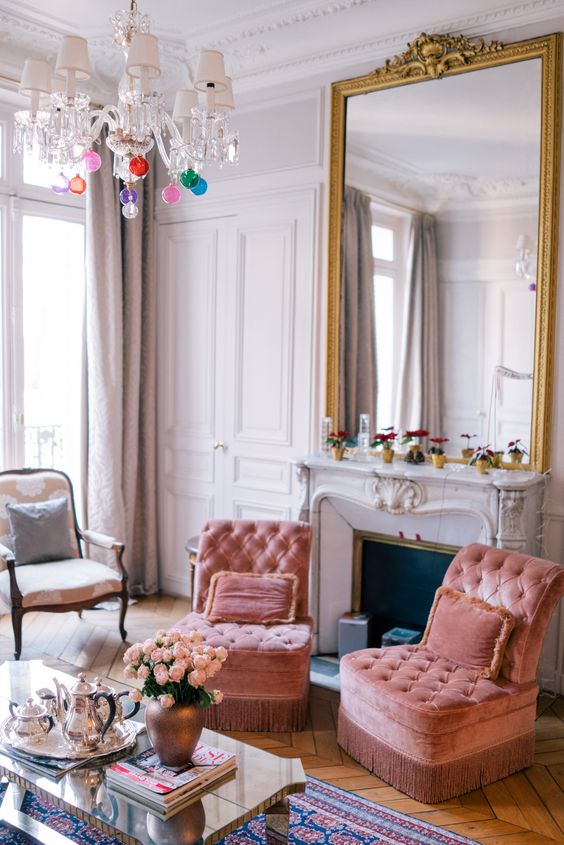 a-bright-and-vivacious-space-with-peachy-pink-chairs-a-fireplace-with-a-large-mirror-over-it-neutral-furniture-and-a-chandelier.jpg